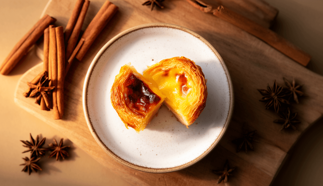 Pastel de Belém dourado com crosta de canela e açúcar caramelizado em prato branco, fotografia profissional